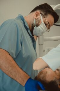 Prosthodontist examining a patient while a denture model and impression tray sit nearby.